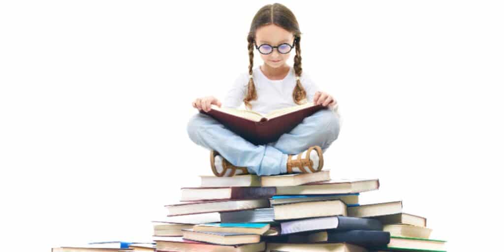 一張小女孩坐在一大堆書上的照片，她的腿上放著一本打開的書，代表著提高文學調查的技巧
