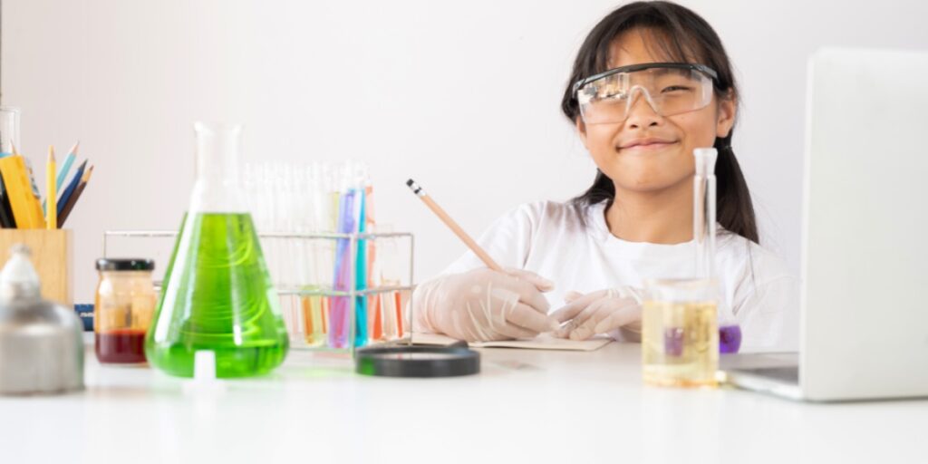 照片上的小女孩穿著實驗服，戴著安全眼鏡，周圍是化學儀器，正在寫一本書，代表整理你的實驗書