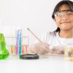 一張年輕女孩穿著實驗室外套和安全眼鏡的照片，周圍是化學設備，並在書中寫作，以代表組織您的實驗室書籍
