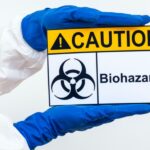 一個人的手臂在危險品套裝中拿著生物危害警告標誌的圖像代表普通實驗室安全標誌
